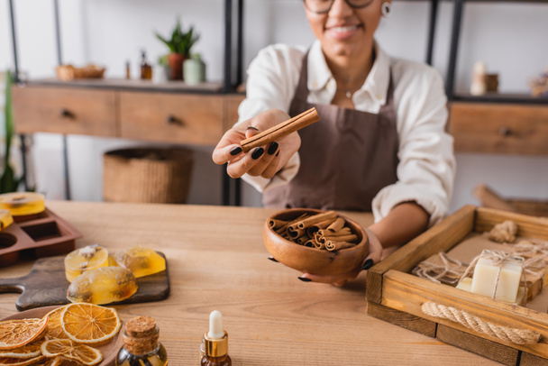 cropped view of smiling african american woman holding cinnamon sticks near handmade soap and dried orange slices - Photo, Image