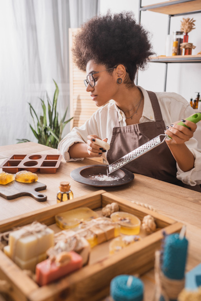 african american woman holding grater near silicone mold and handmade soap in craft workshop - 写真・画像