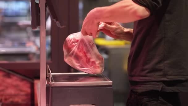 Een man pakt een stuk vers vlees en weegt het op een weegschaal in een winkel. Vleesafdeling - Video