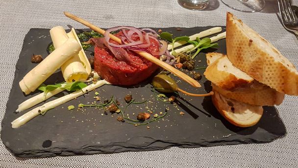 A stony plate with beef tatar and some side dishes. There is toasted bread on the side. Exclusive cuisine. The food is nicely organised on the plate. raw food. - Foto, immagini
