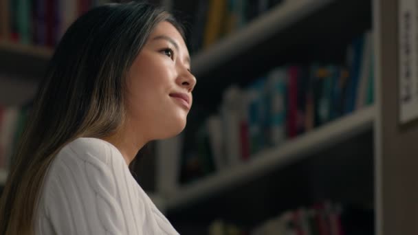 Young korean woman student looking with contemplation at bookshelf in university library in search right textbook concentrated girl in bookstore chooses books from bookcase selects literature to read - Filmagem, Vídeo