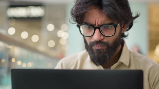 Serious Indian man in glasses looking at laptop screen working online indoors. Close up Arabian businessman in eyeglasses chatting with computer executive analyze business financial data with Internet - Séquence, vidéo