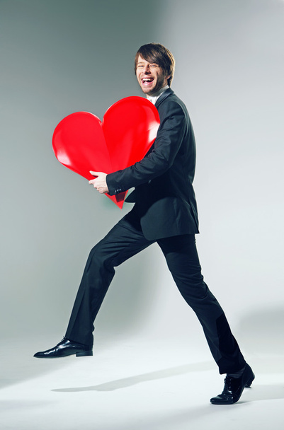 Cheerful young man holding big heart - 写真・画像