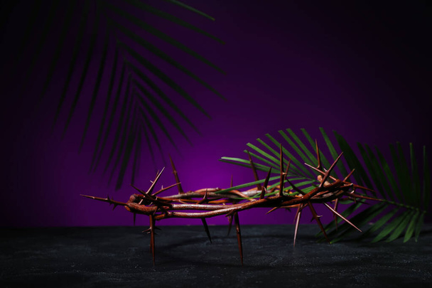 Crown of thorns and palm leaves on table against dark purple background. Good Friday concept - Fotoğraf, Görsel