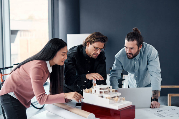 Всем нравится, когда хороший план срабатывает. три молодых архитектора, работающих над макетом современного дома в своем офисе - Фото, изображение