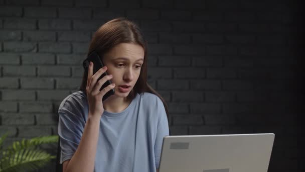 A young female freelancer discusses the details of a working project on the phone. The woman ends the conversation on the phone and starts working on her laptop. High quality 4k footage - Video