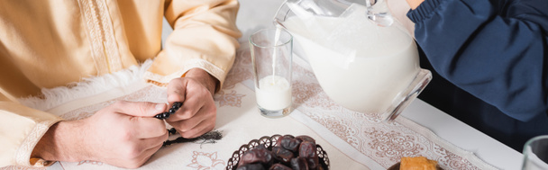 Vista cortada de mulher muçulmana derramando leite perto do marido durante suhur de manhã, banner - Foto, Imagem
