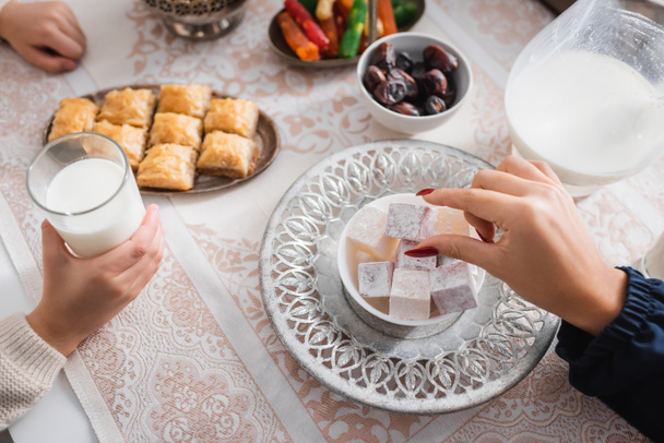 Top view of muslim mother taking turkish delight near son with glass of milk during ramadan  - Foto, Imagem