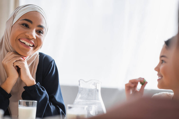 Happy african american mother in hijab looking at blurred kids during suhur at home  - Fotografie, Obrázek