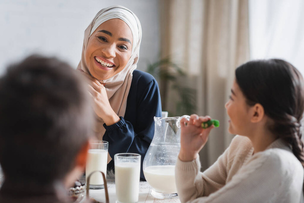 Smiling african american mother in hijab looking at blurred children near suhur food at home  - Foto, Imagem