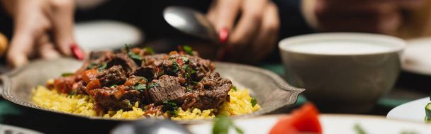 Rajatut näkymä hämärtynyt musliminainen laskemisesta pilaf pöydälle ramadan illallisen aikana, banneri  - Valokuva, kuva