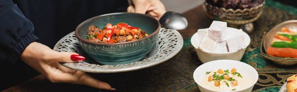 Καλλιεργημένη θέα της γυναίκας μουσουλμάνος κρατώντας νόστιμο πιάτο κατά τη διάρκεια του δείπνου ραμαντάν, πανό  - Φωτογραφία, εικόνα