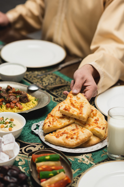 Обрезанный вид мусульманина, принимающего пита-хлеб возле еды во время ужина Рамадан  - Фото, изображение