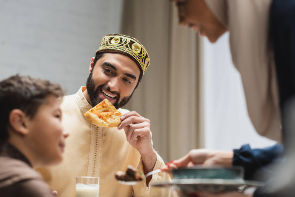 χαρούμενος μουσουλμάνος πατέρας κρατώντας πίτα ψωμί κοντά θολή οικογένεια στο σπίτι  - Φωτογραφία, εικόνα