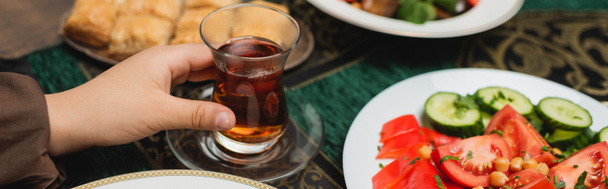 Rajatut näkymät muslimipoika tilalla perinteinen lasi kuppi teetä lähellä iftar ruokaa kotona, banneri  - Valokuva, kuva