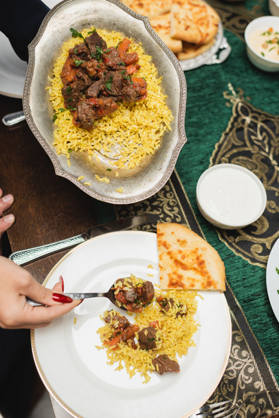 Vue du dessus de la femme musulmane servant pilaf sur l'assiette pendant iftar à la maison  - Photo, image