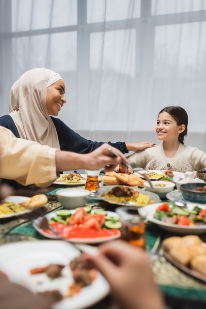 African american mother in hijab looking at daughter near ramadan dinner at home  - Foto, imagen
