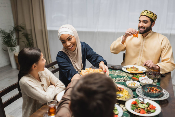 African american mother in hijab holding pita bread near family during ramadan  - Zdjęcie, obraz
