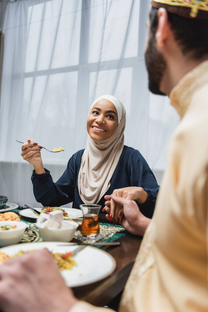 African american woman in hijab holding hand of blurred husband near ramadan dinner at home  - Photo, image