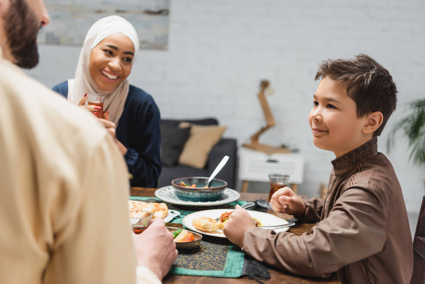 Мусульманские родители смотрят на сына возле вкусного ужина дома  - Фото, изображение