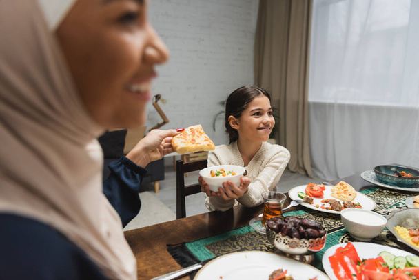 Uśmiechnięta muzułmańska rodzina trzymająca jedzenie podczas ramadan iftar w domu  - Zdjęcie, obraz