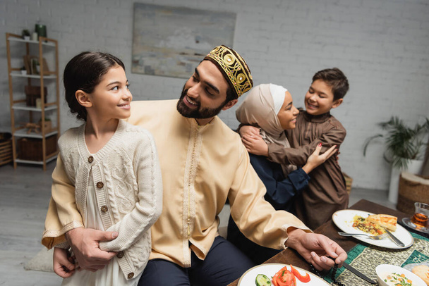 Muslim father hugging daughter near family and ramadan dinner at home  - Foto, Imagen