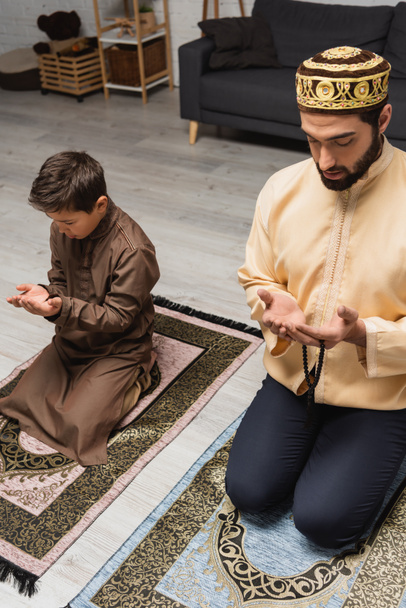 Pai muçulmano com contas de oração orando perto do filho em casa  - Foto, Imagem