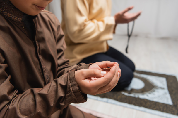 Обрізаний вид мусульманського хлопчика, який молиться під час молитви біля розмитого батька вдома
  - Фото, зображення