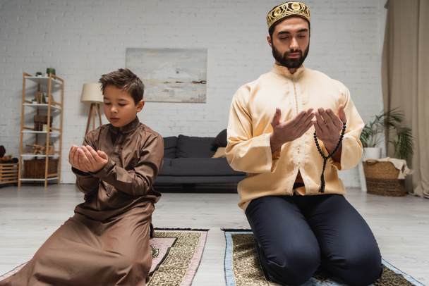 Hombre musulmán e hijo rezando en alfombras durante el ramadán en casa  - Foto, imagen