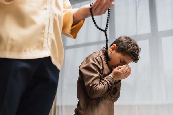 Muslim boy holding hands near face while praying with father at home  - Photo, Image