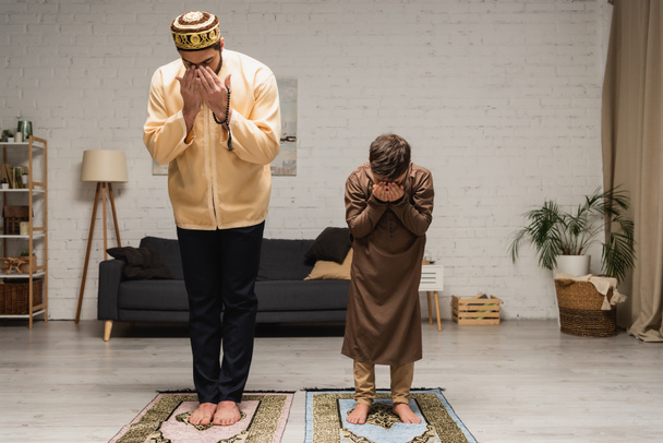 Barefoot muslim father and boy praying on rugs at home  - Photo, image