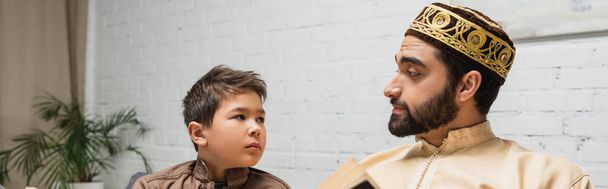 Middle eastern man looking at son near blurred book at home, banner  - Foto, Imagem