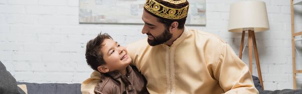 Smiling muslim man hugging preteen son at home, banner  - 写真・画像