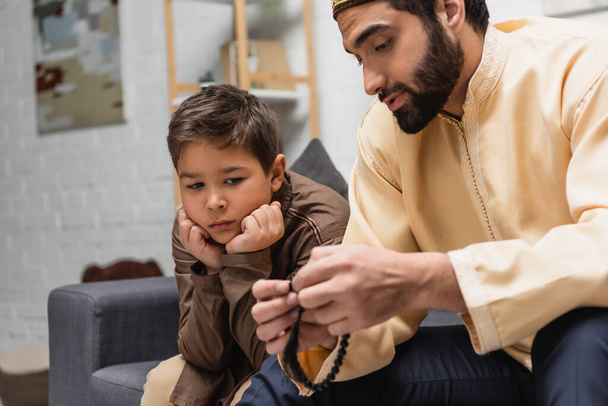 Мусульманин держит дома четки и разговаривает с сыном на диване  - Фото, изображение
