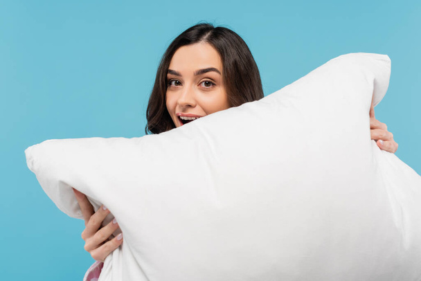 amazed young woman with opened mouth holding white pillow isolated on blue  - Foto, Imagem