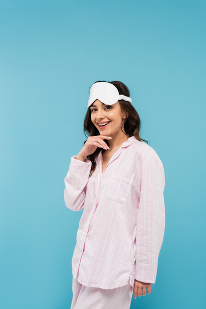happy young woman in night mask and pajamas isolated on blue  - Photo, Image