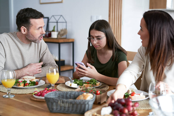 Blanke familie eten lunch en tiener meisje met behulp van mobiele telefoon  - Foto, afbeelding