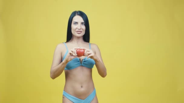 Mooie jonge vrouw met rood hart in de hand op een gele achtergrond poseren om camera in de studio - Video