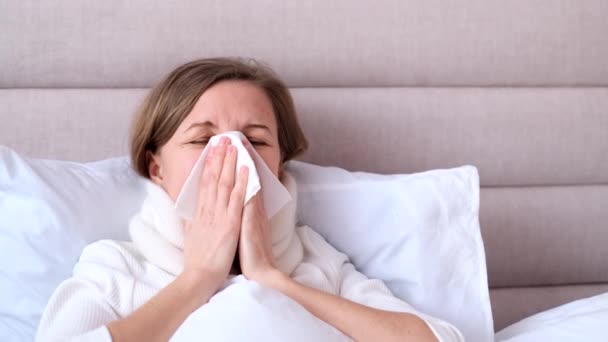 Μια γυναίκα με κρύωμα είναι ξαπλωμένη στο κρεβάτι στο σπίτι. Μια άρρωστη αλλεργική γυναίκα με αλλεργικά συμπτώματα βήχει στο σπίτι. Η έννοια της γρίπης. - Πλάνα, βίντεο