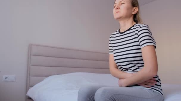 A woman of European appearance, sitting in bed, suffers from stomach pain. Menstrual cycle in a woman. - Video