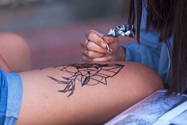 Kazan, Russia - July 10 2018: Tattoo artist drawing a low poly style deer head with henna on a woman's thigh. - Fotografie, Obrázek