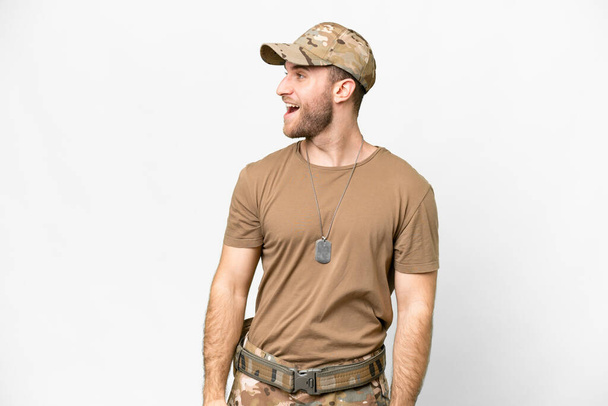 Military with dog tag over isolated white background laughing in lateral position - Photo, Image