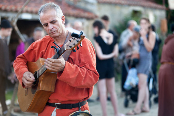 Bazoges-en-Pareds, Francja - 29 lipca 2017: Średniowieczny minstrel grający na gitarze podczas corocznego festiwalu "Nocturnes Medievales". - Zdjęcie, obraz