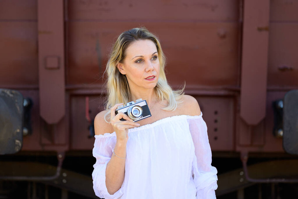 Front view of a amazed middle aged woman holding an old camera and looking aside - Foto, afbeelding