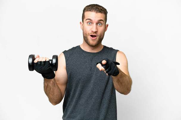 Young sport man making weightlifting over isolated white background surprised and pointing front - Fotografie, Obrázek