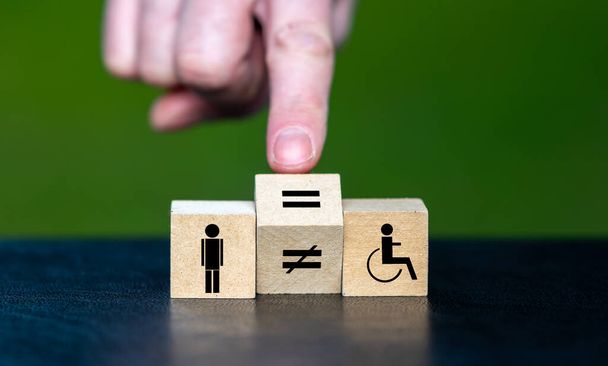 Символ рівних прав осіб з інвалідністю. Рука повертає дерев'яний куб і змінює знак нерівності на знак рівності
. - Фото, зображення