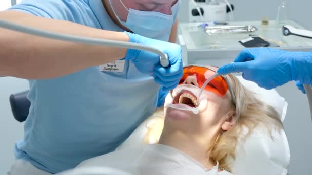 tekutý cofferdam izolovat dásně z působení bělicí prostředek optragat rotační rozmetadlo mytí zubů v zubní klinice s proudem vody a slin ejekce v ústech pacient v ochranných brýlích - Záběry, video