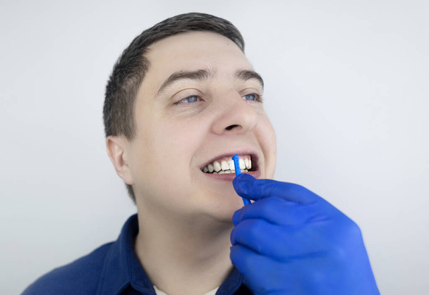 Μεσοδόντια βούρτσα. Ένας άντρας δείχνει μια βούρτσα για τον καθαρισμό του μεσοδόντια χώρου. Βούρτσα για καθαρισμό δοντιών και καθημερινή στοματική φροντίδα. Οδοντιατρική και ορθοδοντική  - Φωτογραφία, εικόνα