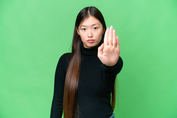 Молодая азиатка на изолированном фоне хромы делает остановку жест - Фото, изображение