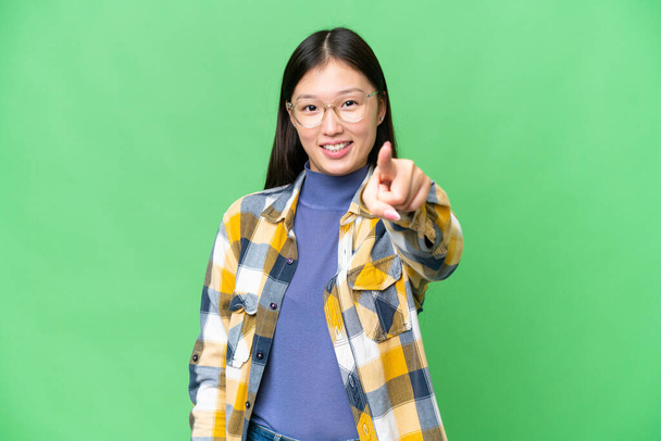 Молодая азиатка на изолированном фоне хрома ключ указывая фронт со счастливым выражением лица - Фото, изображение